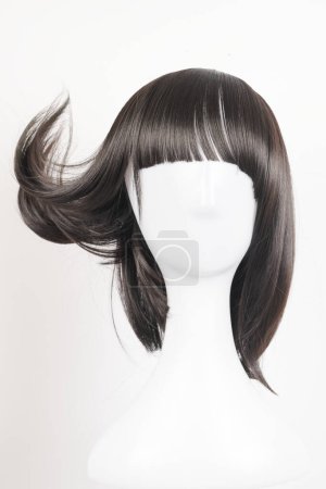 Téléchargez les photos : Perruque noire naturelle sur tête de mannequin blanche. Cheveux raides de longueur moyenne avec frange sur le porte-perruque métallique isolé sur fond blanc, vue de face - en image libre de droit