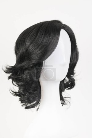 Téléchargez les photos : Perruque noire naturelle sur tête de mannequin blanche. Cheveux bouclés ondulés de longueur moyenne sur le porte-perruque métallique isolé sur fond blanc, vue latérale - en image libre de droit