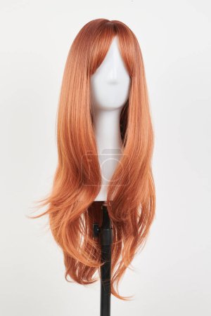 Photo for Natural looking ginger wig on white mannequin head. Long straight hair with wavy curls on the plastic wig holder isolated on white background, front vie - Royalty Free Image
