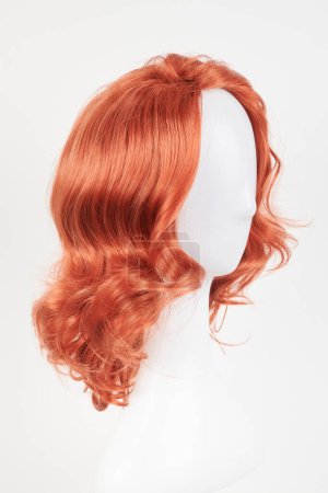 Photo for Natural looking ginger wig on white mannequin head. Medium length hair with wavy curls on the plastic wig holder isolated on white background, side view - Royalty Free Image