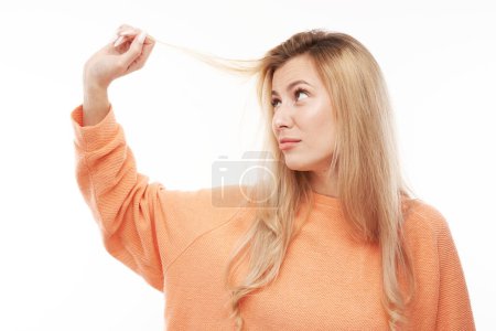 Foto de Retrato mujer joven rubia tocando el pelo con la cara descontenta aislado sobre fondo de estudio blanco, concepto de cabello dañado - Imagen libre de derechos