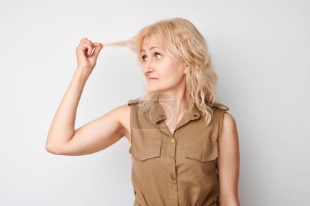 Foto de Portrait of blonde adult woman touching hair with displeased face isolated on white studio background, damaged hair concept - Imagen libre de derechos