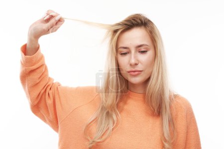 Téléchargez les photos : Portrait jeune femme blonde touchant les cheveux avec le visage mécontent isolé sur fond de studio blanc, concept de cheveux abîmés - en image libre de droit