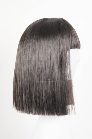 Photo for Natural looking black wig on white mannequin head. Medium length straight hair with bangs on the metal wig holder isolated on white background, side view - Royalty Free Image