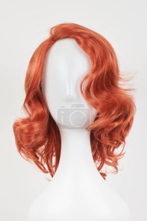 Photo for Natural looking ginger wig on white mannequin head. Medium length hair with wavy curls on the plastic wig holder isolated on white background, front vie - Royalty Free Image