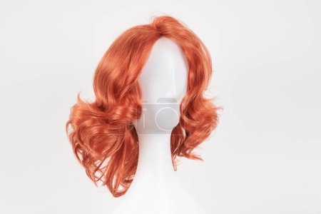 Photo for Natural looking ginger wig on white mannequin head. Medium length hair with wavy curls on the plastic wig holder isolated on white background, front vie - Royalty Free Image
