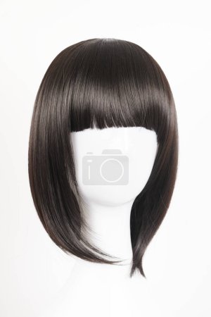 Téléchargez les photos : Perruque noire naturelle sur tête de mannequin blanche. Cheveux raides de longueur moyenne avec frange sur le porte-perruque métallique isolé sur fond blanc, vue de face - en image libre de droit