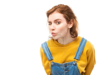 Photo for Portrait of young redhead woman in yellow casual suspiciously looking at camera isolated on white studio background, squinting incredulously - Royalty Free Image