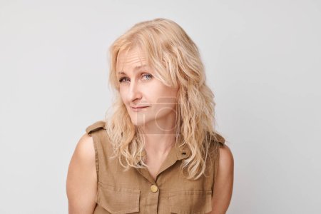 Téléchargez les photos : Portrait de femme mature blonde regardant avec suspicion la caméra isolée sur fond de studio blanc, plissant incrédule - en image libre de droit