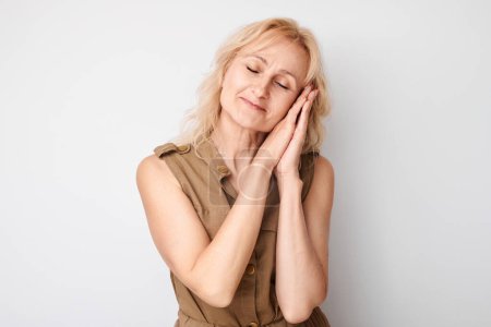 Photo for Studio portrait blonde adult woman put palms under head pretending to sleep isolated on white background - Royalty Free Image