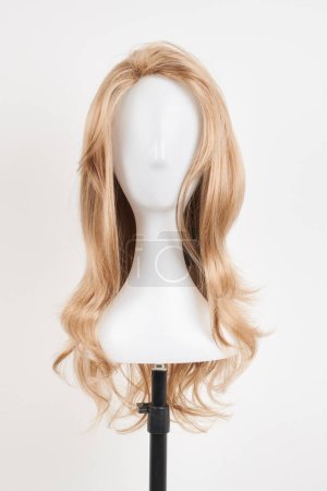 Téléchargez les photos : Perruque blonde naturelle sur tête de mannequin blanche. Cheveux longs sur le porte-perruque en plastique isolé sur fond blanc, face avant - en image libre de droit