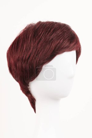 Téléchargez les photos : Perruque brune rouge naturelle sur tête de mannequin blanche. Cheveux foncés de longueur moyenne sur le porte-perruque en plastique isolé sur fond blanc - en image libre de droit