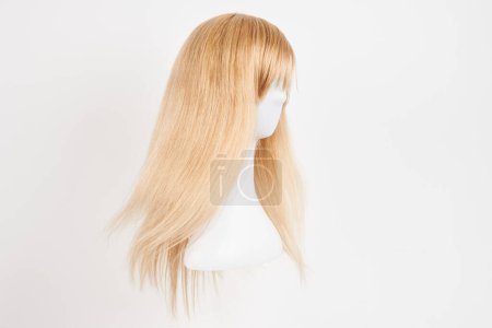 Photo for Natural looking blonde wig on white mannequin head. Long hair on the plastic wig holder isolated on white background, side vie - Royalty Free Image