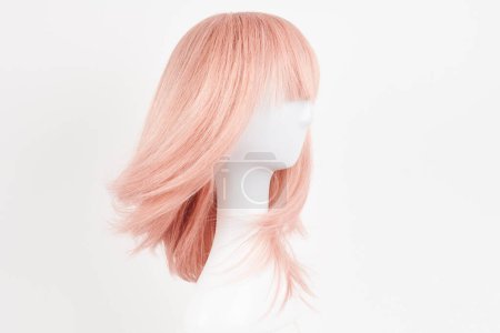 Foto de Peluca rubia rosa de aspecto natural en la cabeza del maniquí blanco. Corte de pelo largo en el soporte de peluca de plástico aislado sobre fondo blanco - Imagen libre de derechos