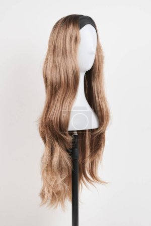 Photo for Natural looking dark blonde wig on white mannequin head. Long fair hair cut on the plastic wig holder isolated on white background - Royalty Free Image