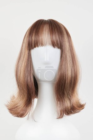 Natural looking dark brunet wig on white mannequin head. Middle length brown hair on the plastic wig holder isolated on white background, front view