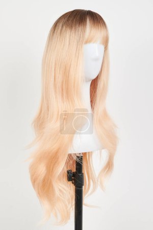 Téléchargez les photos : Perruque blonde naturelle sur tête de mannequin blanche. Cheveux longs sur le porte perruque en plastique isolé sur fond blanc - en image libre de droit