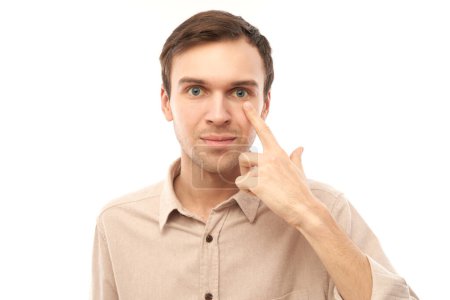 Porträt eines jungen Mannes zeigt mit dem Finger auf sein Auge isoliert auf weißem Studiohintergrund. Vision Check und Verlust des Sehvermögens Konzept, Brillengeschäft