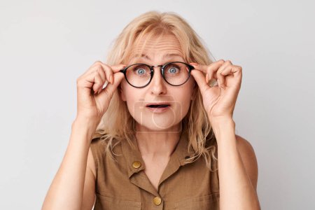 Téléchargez les photos : Portrait de dame de 50 ans qui plisse dans des lunettes isolées sur fond de studio blanc. Vérification de la vision et perte de la vue, concept de recherche, lunettes sho - en image libre de droit