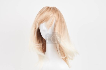 Téléchargez les photos : Perruque blonde naturelle sur tête de mannequin blanche. Cheveux longs sur le porte perruque en plastique isolé sur fond blanc - en image libre de droit