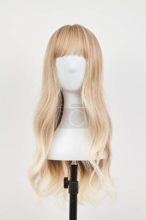 Photo for Natural looking blonde wig on white mannequin head. Long hair on the plastic wig holder isolated on white background, front vie - Royalty Free Image