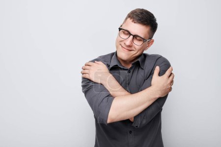 Portrait of caucasian man hugs oneself smiling carefree and happy isolated on white studio background. Self love, self care, mental health concept