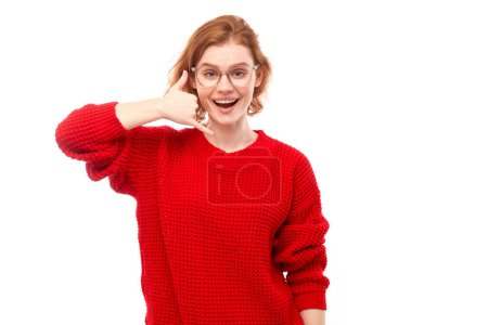 Téléchargez les photos : Portrait de jeune femme rousse feint d'appeler quelqu'un, me fait appeler signe geste avec les doigts isolés sur fond de studio blanc. Appelle-moi, main en forme de téléphone. - en image libre de droit