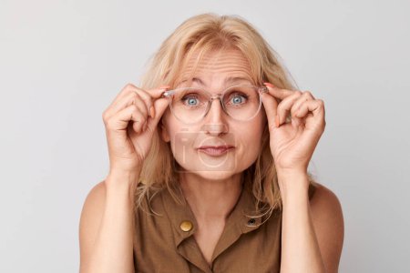 Foto de Retrato de una señora de 50 años entrecerrando los ojos aislada sobre fondo blanco del estudio. Revisión de la visión y pérdida de la vista, concepto de búsqueda, gafas sho - Imagen libre de derechos