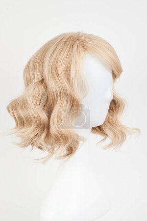 Téléchargez les photos : Perruque blonde blonde naturelle sur tête de mannequin blanche. Cheveux mi-longs coupés sur le porte-perruque en plastique isolé sur fond blanc - en image libre de droit