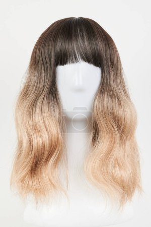 Natural looking blonde fair wig on white mannequin head. Middle length hair cut on the plastic wig holder isolated on white background, front vie