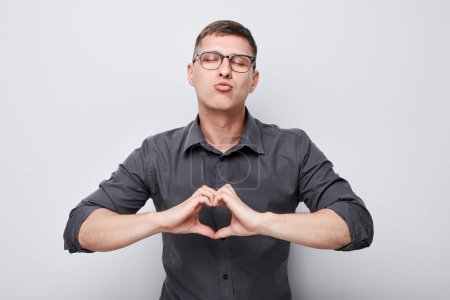 Téléchargez les photos : Portrait de jeune homme d'affaires envoyant des baisers d'air tenant la main en forme de cœur isolé sur fond de studio blanc - en image libre de droit