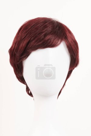 Photo for Natural looking red brunet wig on white mannequin head. Middle length dark hair on the plastic wig holder isolated on white backgroun - Royalty Free Image