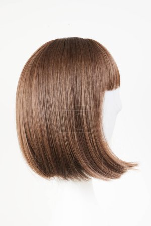 Natural looking dark brunet wig on white mannequin head. Middle length brown hair on the plastic wig holder isolated on white background, side vie