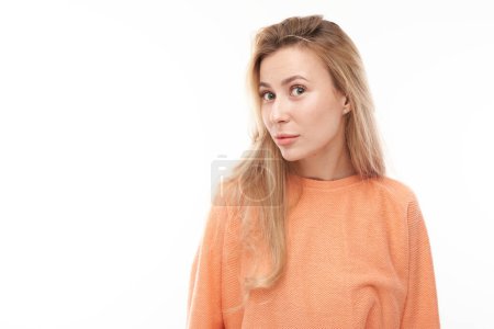 Foto de Retrato de una joven rubia mirando sospechosamente a la cámara aislada sobre fondo blanco del estudio, entrecerrando los ojos incrédulo - Imagen libre de derechos