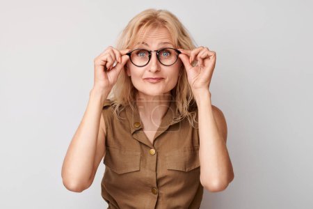 Téléchargez les photos : Portrait de dame de 50 ans qui plisse dans des lunettes isolées sur fond de studio blanc. Vérification de la vision et perte de la vue, concept de recherche, lunettes sho - en image libre de droit