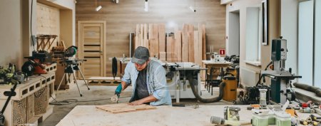 Téléchargez les photos : Charpentier travaille avec du bois dans un atelier de menuiserie. Homme faisant de la menuiserie professionnellement - en image libre de droit