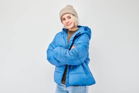 Portrait Caucasian young blond woman smiling joyfully isolated on white studio background. Happy girl in winter blue jacket and hat with glad face expression