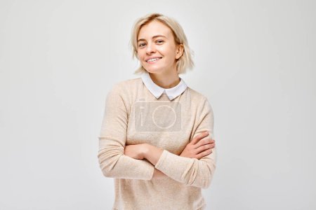 Téléchargez les photos : Portrait Femme blanche jeune blonde souriante joyeusement isolée sur fond de studio blanc. Fille heureuse en chemisier beige avec expression joyeuse du visage - en image libre de droit