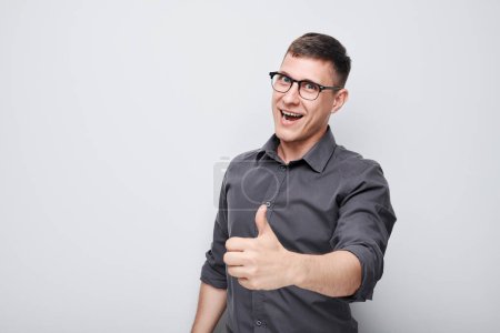 Téléchargez les photos : Portrait de jeune homme caucasien souriant montrant joyeusement les pouces vers le haut geste isolé sur fond de studio blanc. Approuve le bon choix, la bonne décision - en image libre de droit