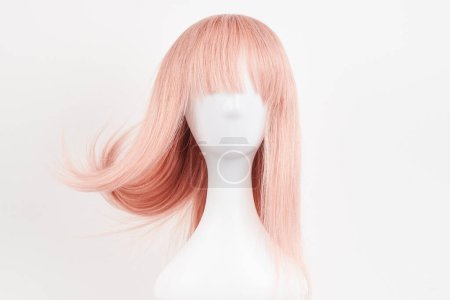 Téléchargez les photos : Perruque blonde rose à l'aspect naturel sur tête de mannequin blanche. Cheveux longs coupés sur le support de perruque en plastique isolé sur fond blanc - en image libre de droit