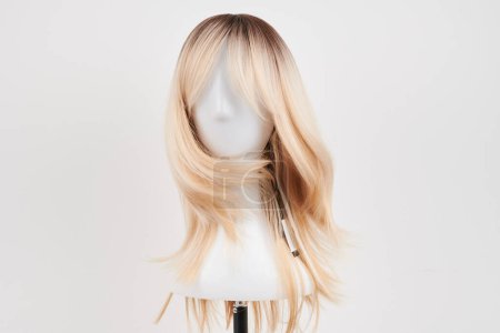 Téléchargez les photos : Perruque blonde naturelle sur tête de mannequin blanche. Cheveux longs sur le porte-perruque en plastique isolé sur fond blanc, face avant - en image libre de droit