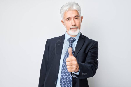 Photo for Portrait of mature man in business suit smiling joyfully showing thumbs up gesture isolated on white studio background. Approves good choice, right decision - Royalty Free Image