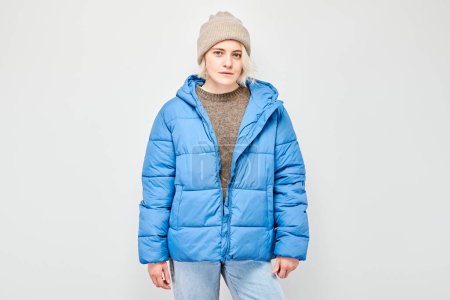 Photo for Portrait Caucasian young blond woman smiling joyfully isolated on white studio background. Happy girl in winter blue jacket and hat with glad face expression - Royalty Free Image