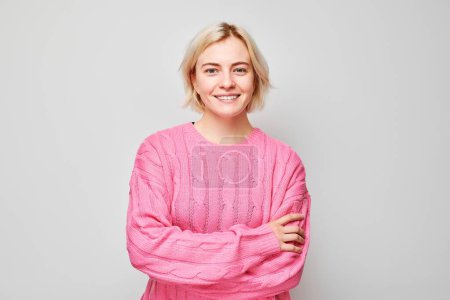 Téléchargez les photos : Portrait Femme blanche jeune blonde souriante joyeusement isolée sur fond de studio blanc. Fille heureuse en pull rose avec expression de visage heureux - en image libre de droit