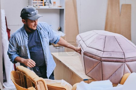 Photo for Carpenter works makes pink velvet coffin in carpentry workshop. Man doing furniture professionall - Royalty Free Image