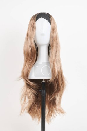 Photo for Natural looking dark blonde wig on white mannequin head. Long fair hair cut on the plastic wig holder isolated on white background - Royalty Free Image