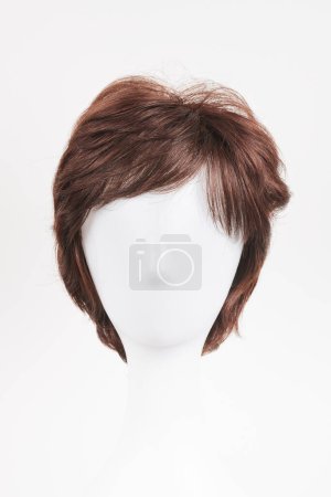 Natural looking dark brunet wig on white mannequin head. Short brown hair on the plastic wig holder isolated on white background, front view 