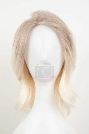 Photo for Natural looking blonde fair wig on white mannequin head. Middle length hair cut on the plastic wig holder isolated on white background, front vie - Royalty Free Image