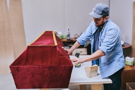 Photo for Carpenter works makes red velvet coffin in carpentry workshop. Man doing furniture professionall - Royalty Free Image