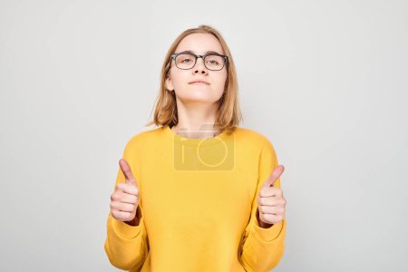 Foto de Retrato de una joven estudiante sonriendo alegremente mostrando un gesto de pulgares hacia arriba aislado sobre fondo blanco del estudio. Aprueba la buena elección, la decisión correcta - Imagen libre de derechos